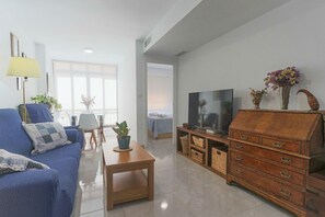 A living room with a blue sofa, a wooden coffee table, a TV stand, and a cabinet. - 097 - Club Náutico 012 - comfortHOLIDAYS (Santa Pola)