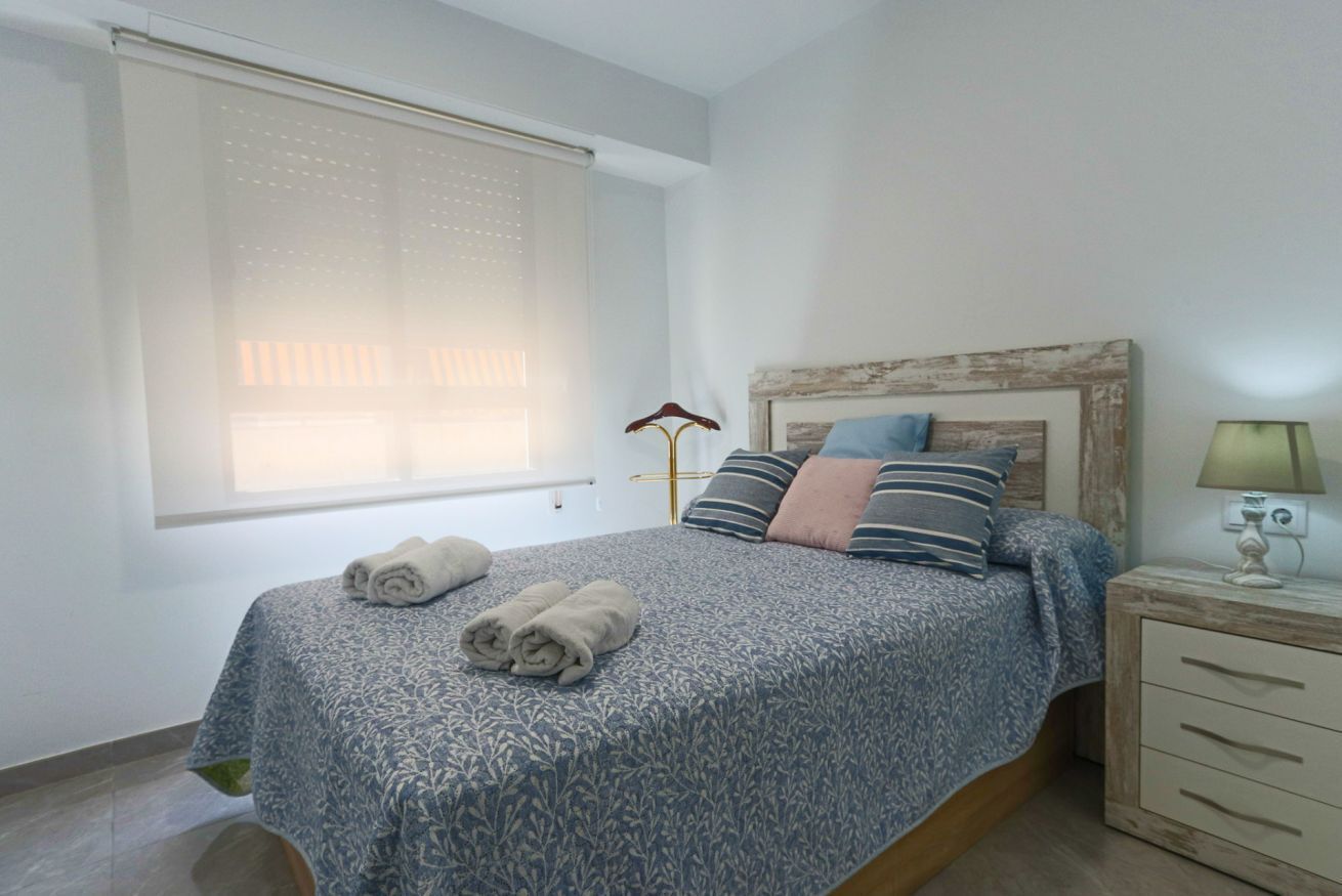 A bedroom with a bed, a bedside table, a lamp, and a window with blinds.