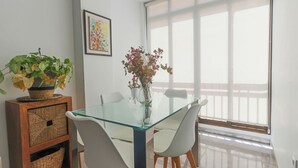 A dining area with a glass table, white chairs, a wooden sideboard with baskets, a vase with flowers, and a large window with a view. - 097 - Club Náutico 012 - comfortHOLIDAYS (Santa Pola)