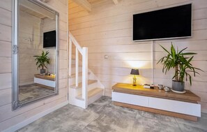 Stylish living area with a large mirror, staircase, flat-screen TV, and potted plants.