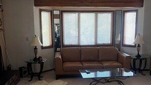 A living room with a brown leather sofa, a glass coffee table, and a fluffy rug. There are two lamps on side tables, and a ceiling fan is visible.