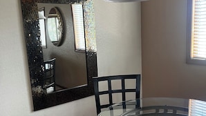A dining area with a glass table, black chairs, a decorative mirror, and a pendant light.