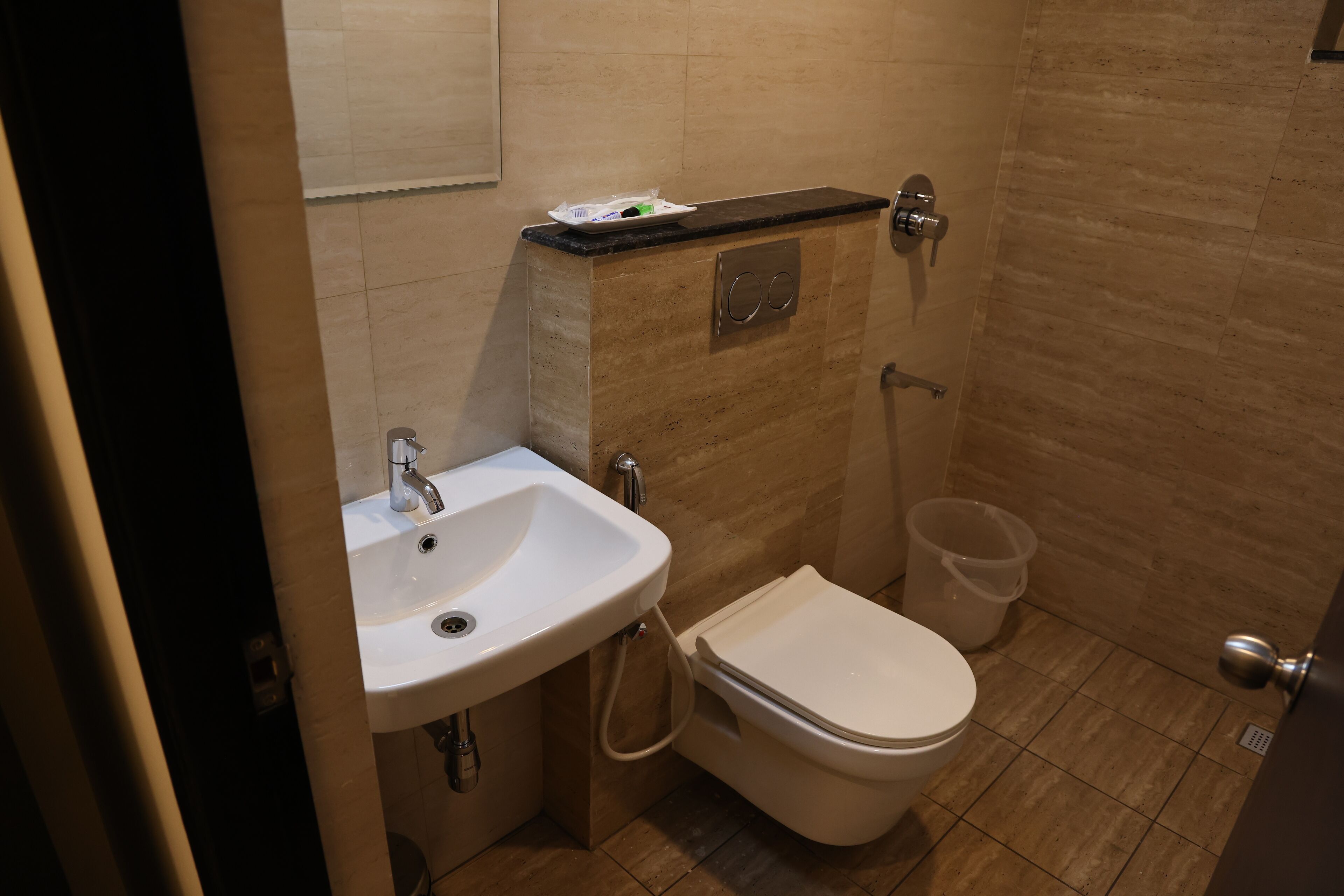 A compact bathroom with a sink, toilet, and a small trash bin.