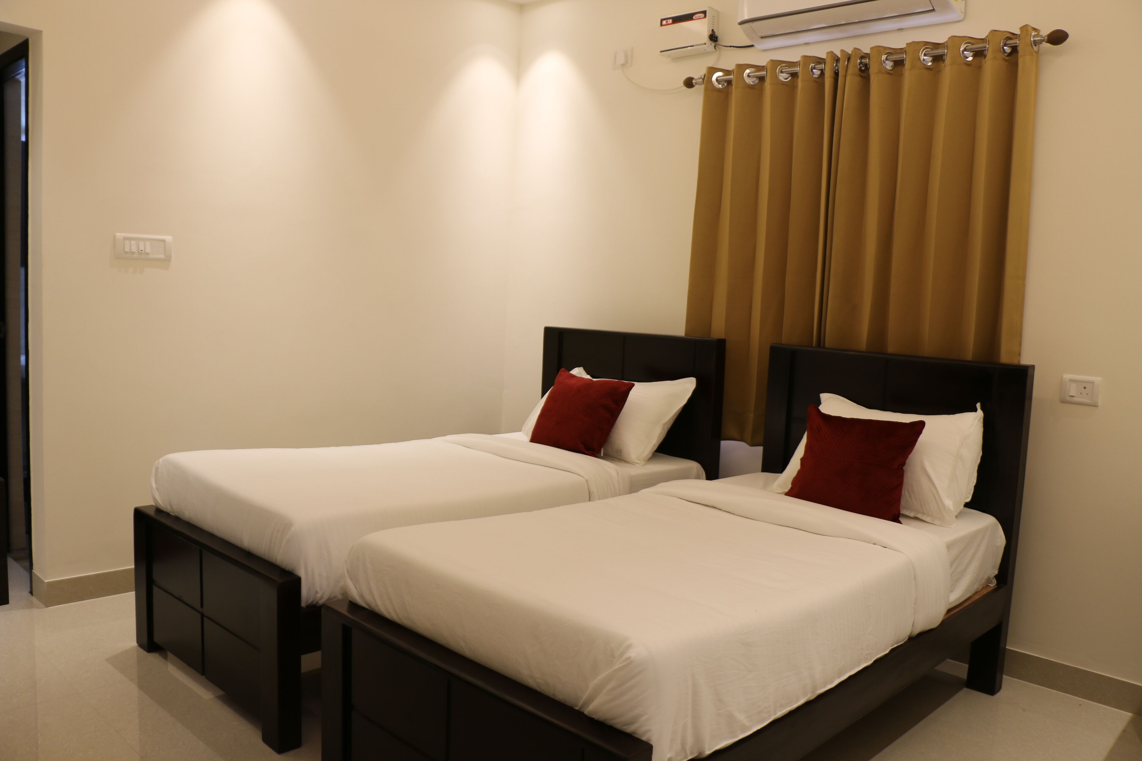 Une chambre d’hôtel avec deux lits simples, une tête de lit sombre, un mur de couleur beige et un rideau marron.