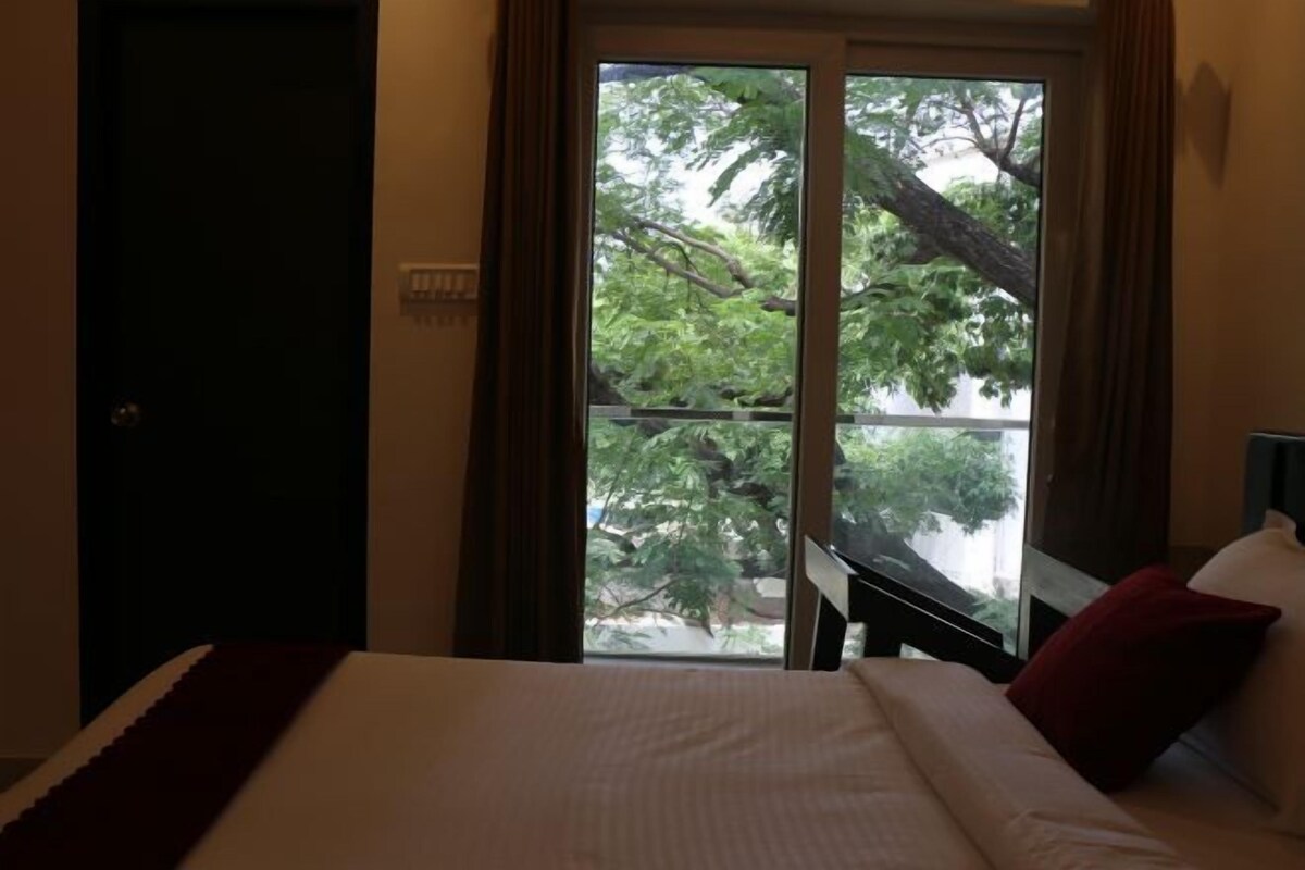 Una habitación de hotel con cama, ventana con cortinas y vistas a árboles.