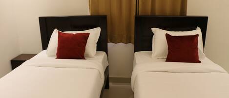 Two single beds with white bedding and red pillows, a nightstand, and a brown curtain.