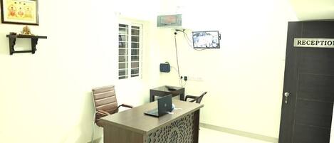 A reception area with a desk, chairs, a door labeled "RECEPTION", a wall-mounted TV, and a framed picture.