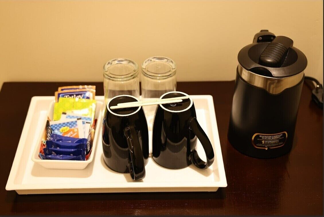 A tray with two black coffee mugs, two salt and pepper shakers, and a container of snacks on a white tray.