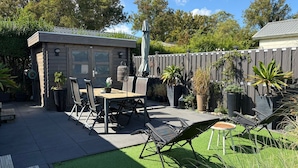 Un espace patio avec une table et des chaises, un petit abri de jardin et un jardin clôturé.