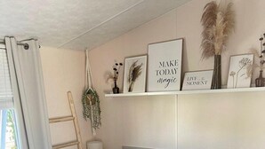 Ein Schlafzimmer mit Bett, Nachttisch, Lampe, einem Regal mit Dekoration und einem Fenster mit Vorhängen.