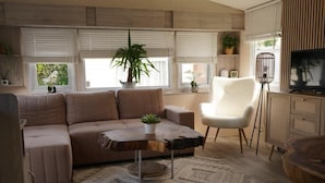 Un salon moderne avec un canapé d’angle, un fauteuil blanc, une table basse et un téléviseur.