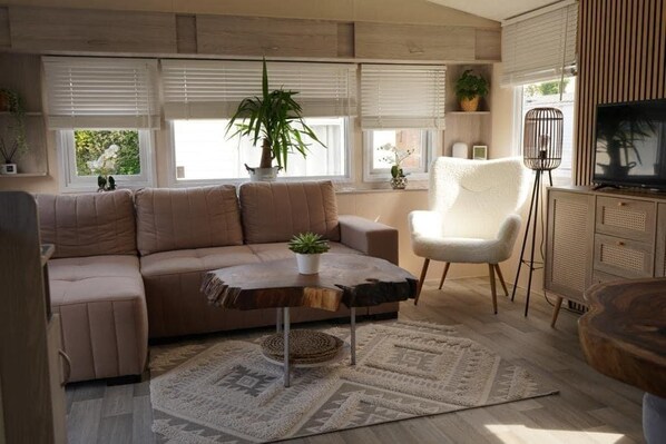 Una sala moderna con un sofá seccional, un sillón blanco, una mesa de centro y un televisor.
