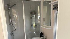 Ein kleines Badezimmer mit einer Duschkabine, einem weißen Waschbecken und einer Toilette.