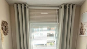 Une chambre de taille modeste, équipée de deux lits, d’une fenêtre avec stores et d’un petit luminaire fixé au mur.