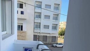 A narrow balcony with a tiled floor, a clothesline with a few items, and a view of a street with buildings and a white car. - Apartment 5 minutes' walk from the beach (martil)