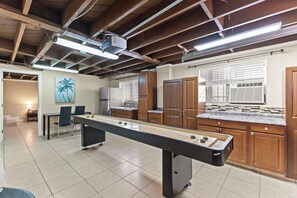 A pool table in a room with wooden cabinets, a kitchen area, and a painting of palm trees.