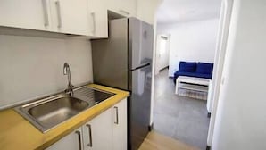 Una cocina compacta con un lavamanos de acero inoxidable, un refrigerador y armarios blancos.