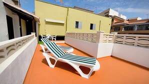 Una terraza en la azotea con dos sillones blancos y una mesita, barandal blanco y un edificio amarillo al fondo.