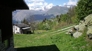 Un chalet de montagne rustique, avec une façade en pierre, une porte en bois et une vue sur des montagnes enneigées au loin.
