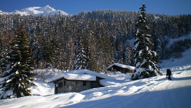 Un paysage montagneux enneigé, avec un bâtiment en pierre et des arbres couverts de neige.