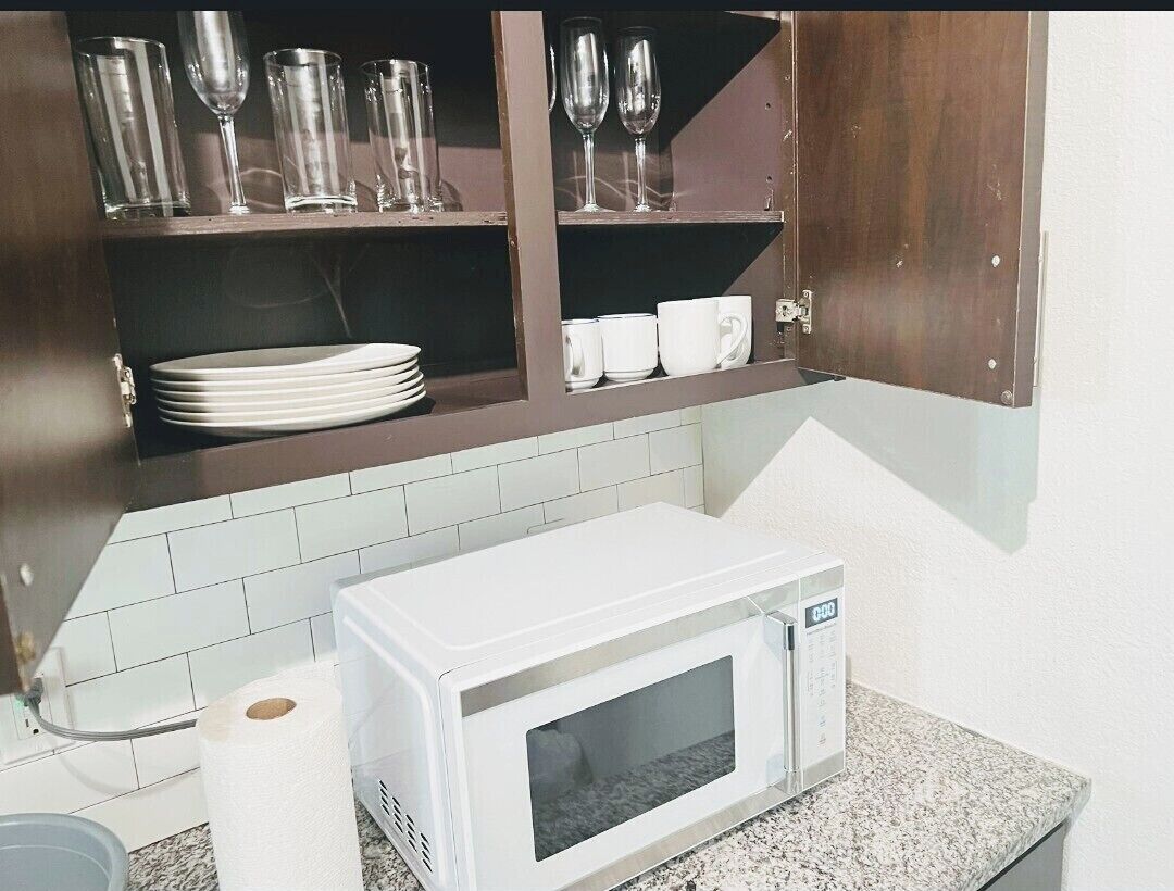 Une cuisine avec un four à micro-ondes blanc, un meuble contenant de la vaisselle et des assiettes, et un rouleau d’essuie-tout.