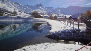 Schneebedeckte Landschaft mit klarem See, Bergen im Hintergrund und einem Holzzaun am Ufer.