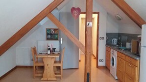 A small, cozy attic room with a wooden dining table and chairs, a kitchen with wooden cabinets, and a visible radiator. - ECOLE A GITER - NID D'AIGLE (SAINT FRANCOIS DE SALES)