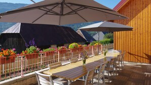 An outdoor patio with wooden tables and chairs, a large umbrella, and flower planters along the railing. - ECOLE A GITER - NID D'AIGLE (SAINT FRANCOIS DE SALES)