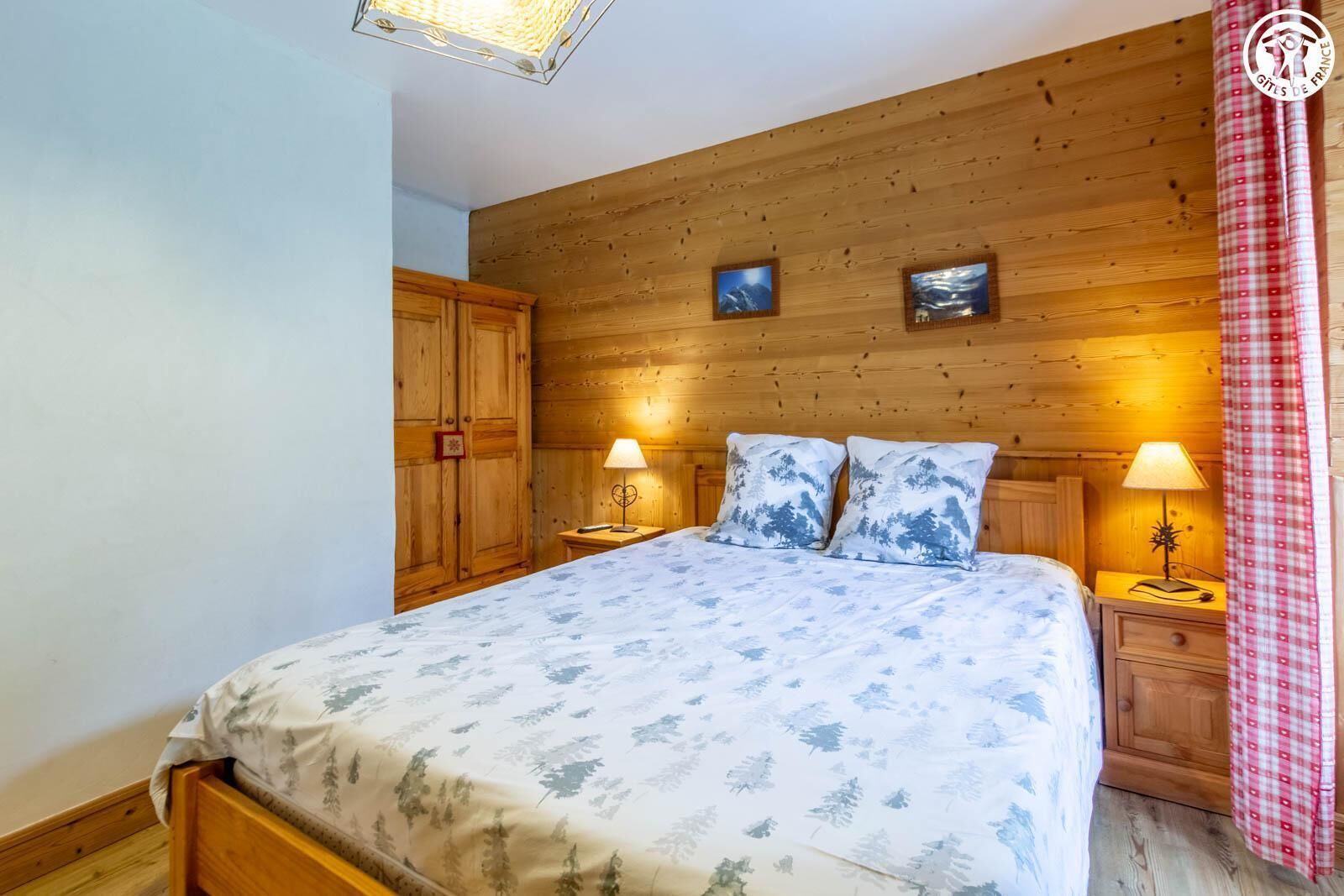 Une chambre à coucher avec une tête de lit en bois, deux lampes de chevet, un lit recouvert d’une couvre-lit à motifs floraux et une armoire en bois.