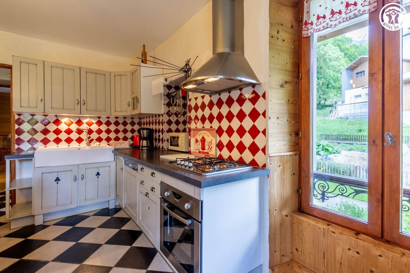 A kitchen with white cabinets, a black and white checkered floor, a gas stove, and a window with a view of greenery.