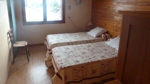 A small, cozy room with two beds, a wooden ceiling, a window, and a chair.