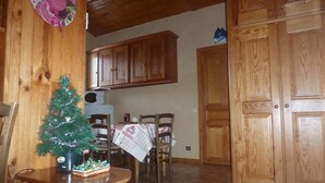 A wooden dining area with a small Christmas tree, a table with a tablecloth, and wooden cabinets in the background.