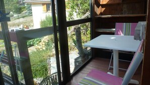 A small room with a white table and a striped chair, large windows with a view of a mountainous area and houses.