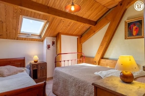 A cozy attic bedroom with two beds, a skylight, wooden beams, and a painting on the wall.