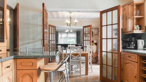 Una cocina con armarios de madera, un comedor con mesa y sillas, y una cafetera sobre la encimera.