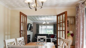 Un comedor con una mesa de madera y sillas blancas, un sofá al fondo y una araña.