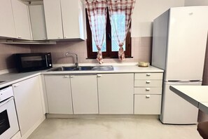 A kitchen with white cabinets, a microwave, a sink, a refrigerator, and a window with curtains.
