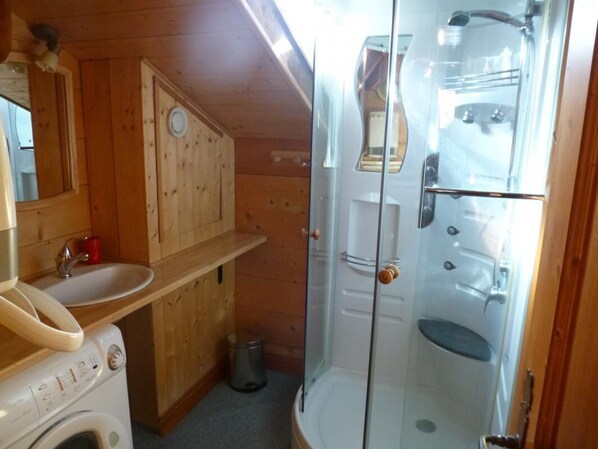 A compact bathroom with a washing machine, sink, and glass-enclosed shower.