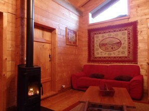 A cozy room with a wooden interior, a red sofa, a table, and a wood-burning stove.