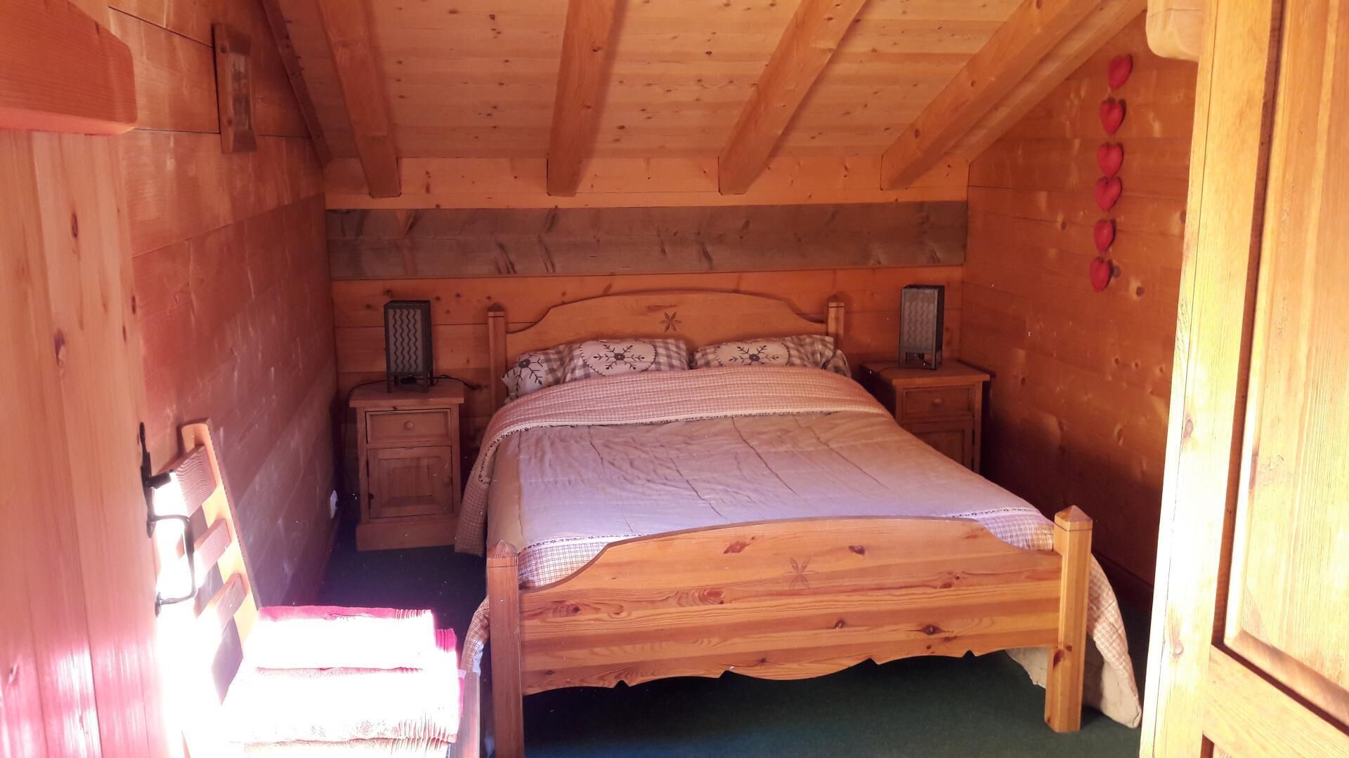 Camera da letto in una baita di legno con un letto singolo, due comodini e un tavolino da notte.