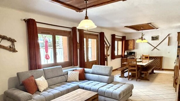 Een woonkamer met een hoekbank, een houten salontafel, een eettafel met stoelen, en een keuken in de achtergrond.