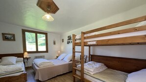 Een kamer met drie stapelbedden, een raam met uitzicht op groen, een houten plafond en een wandplank met spullen.