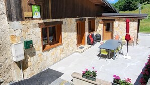 Een rustiek chalet met stenen muren, houten balken en een terras met zitplaatsen.