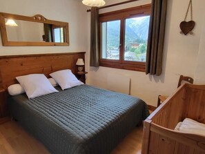 Un dormitorio con cabecera de madera, cama con almohadas blancas, ventana con vistas a montañas y una cuna de madera.