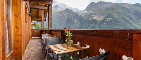 A wooden deck with tables and chairs, overlooking a mountainous landscape.