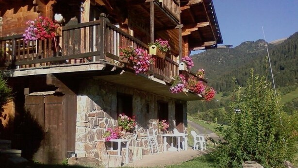 Un chalet de madera con balcones decorados con flores, paredes de piedra y vistas a un paisaje montañoso.