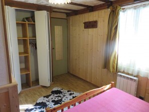 Makuuhuoneessa on puulattia, vaaleanpunaisella peitteellä varustettu sänky, lehmännahkamatto, puinen vaatekaappi ja patteri.