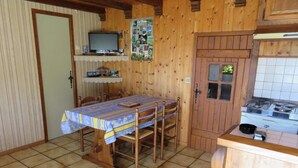 Un interior de madera con una mesa de comedor, sillas, un televisor, una zona de cocina con estufa y una puerta con ventanal.