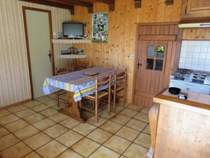 Ein Holzinterieur mit einem Esstisch, Stühlen, einem Fernseher, einer Küchenzeile mit Herd und einer Tür mit Fenster.