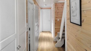A narrow hallway with wooden walls and white doors, leading to a staircase.